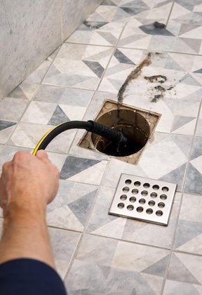 Plumber using drain snake to inspect bathroom floor drain during leak detection service