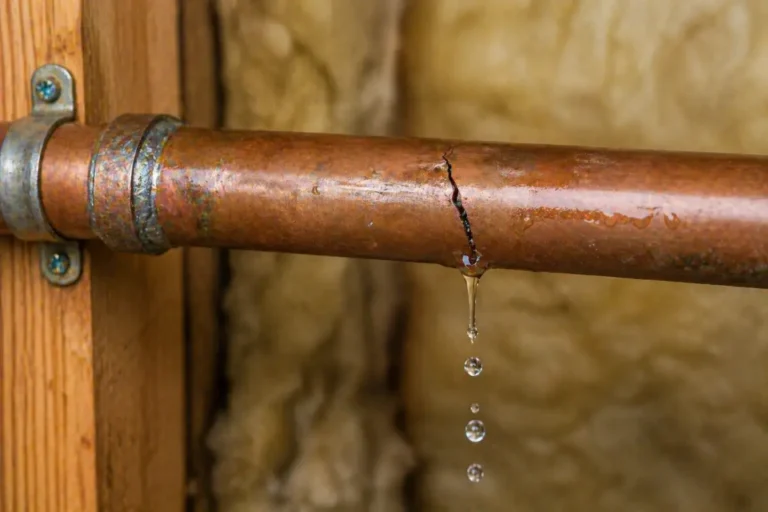 Close-up of a cracked copper pipe leaking water with visible dripping